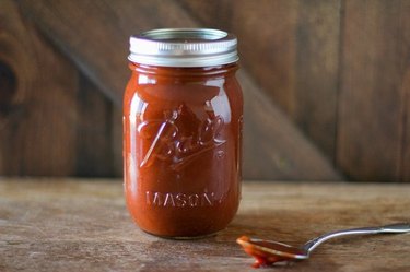 A mason jar full of barbecue sauce next to a spoon