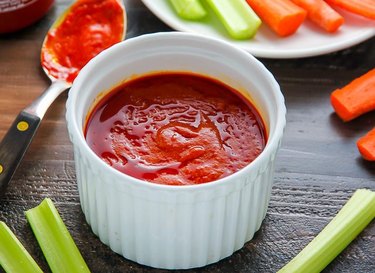 A white bowl filled with buffalo sauce surrounded by carrots and celery