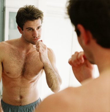 close-up of a man brushing his teeth and looking in the mirror