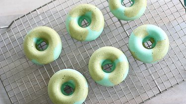 Blue and green donuts cooling on rack