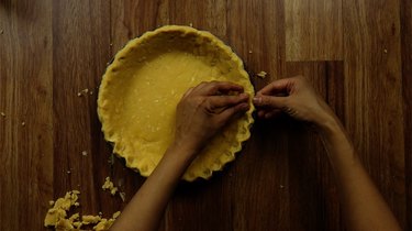 Preparing gluten-free, low-carb coconut flour rolled pie crust for baking by fluting edges.