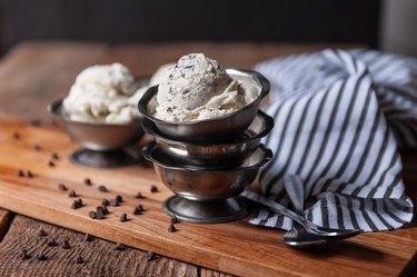 A stack of silver bowls topped with chocolate chip ice cream next to a striped tea towel