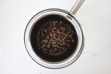 Finely chopped dark chocolate set in a heatproof bowl and saucepan.