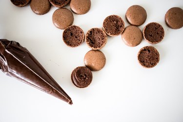 Chocolate macaron shells being filled with ganache.