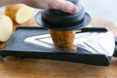 slicing a potato on a mandolin slicer