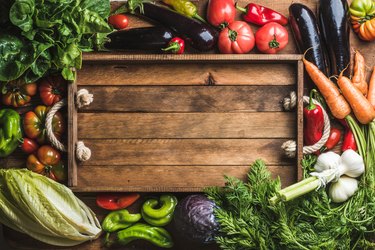 Fresh raw vegetable ingredients for healthy cooking or salad making with rustic wooden tray in center, top view, copy space. Diet or vegetarian food concept, horizontal composition