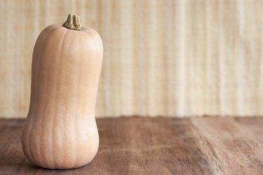 A single whole, uncooked buttercup squash standing upright on a textured brown surface, with a textured beige background