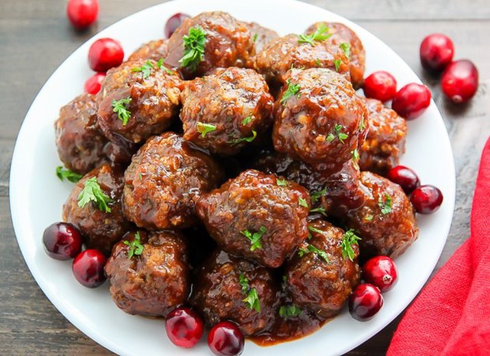 Meatballs in cranberry sauce on a white plate, garnished with whole berries and chopped parsley