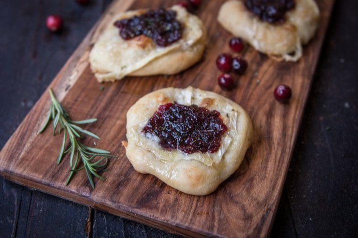 Cranberry brie flatbreads on a dark wood cutting board, with whole berries and a sprig of rosemary