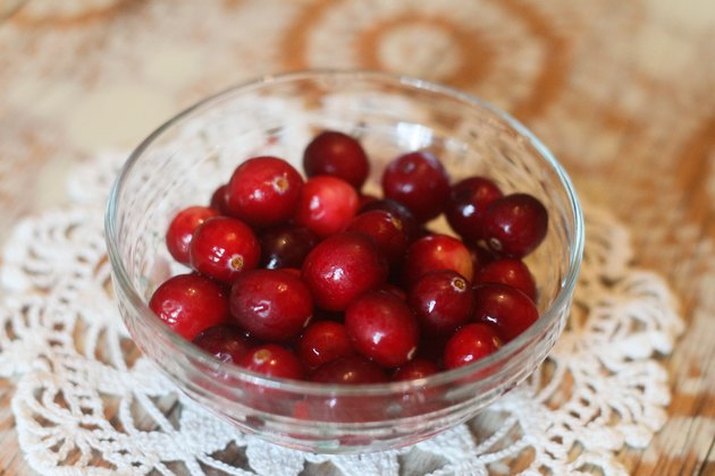 A small glass bowl of whole cranberries on a crocheted white toily