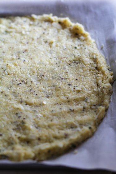 Raw cauliflower pizza crust on baking sheet.