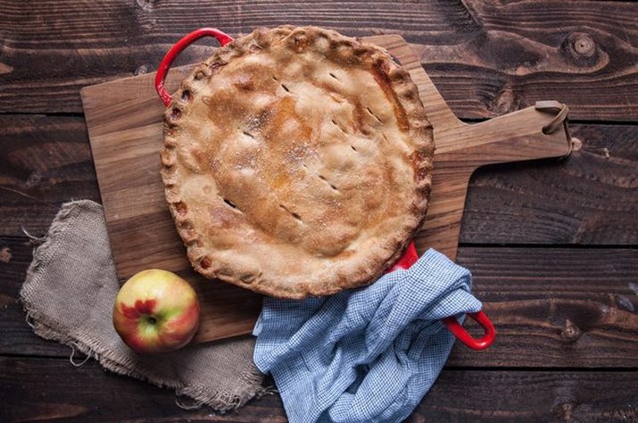 An apple pie baked in a cast iron skillet on a wood background