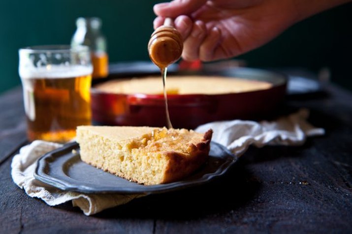 A slice of cornbread on a tin plate being drizzled with honey