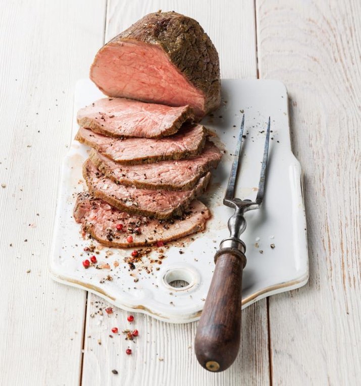 Roast beef and meat fork on white wooden background