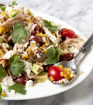 A healthy salad featuring tomatoes, avocados, cilantro, charred corn, chicken and cheese.