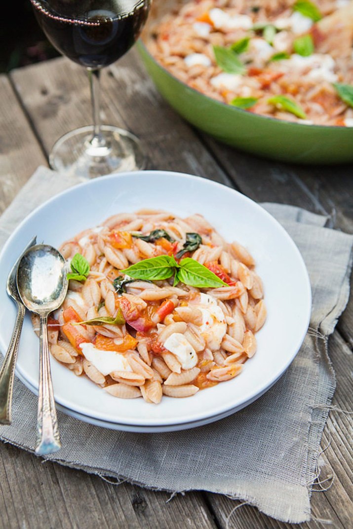 A bowl of Caprese pasta topped with fresh basil, served with a glass of red wine