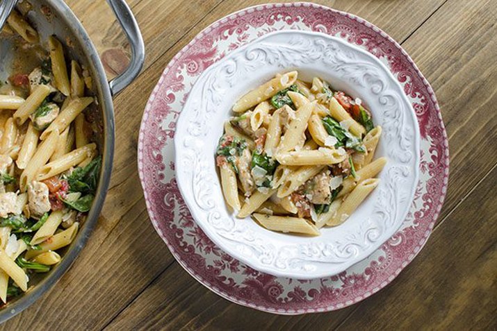 A bowl of freshly made chicken and spinach skillet pasta, topped with grated Parmesan cheese