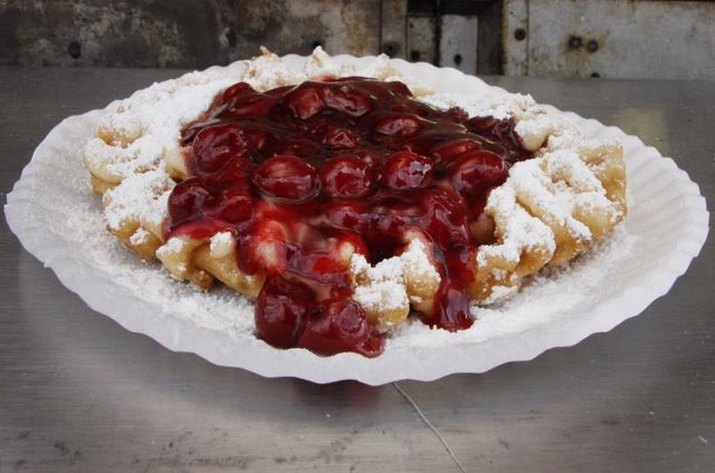 Golden funnel cake drizzled with powdered sugar and fresh strawberries.