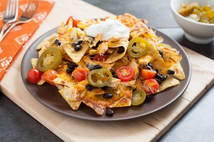 A plate of shredded chicken, jalapenos, tomatoes, black beans and sour cream on a bed of tortilla chips